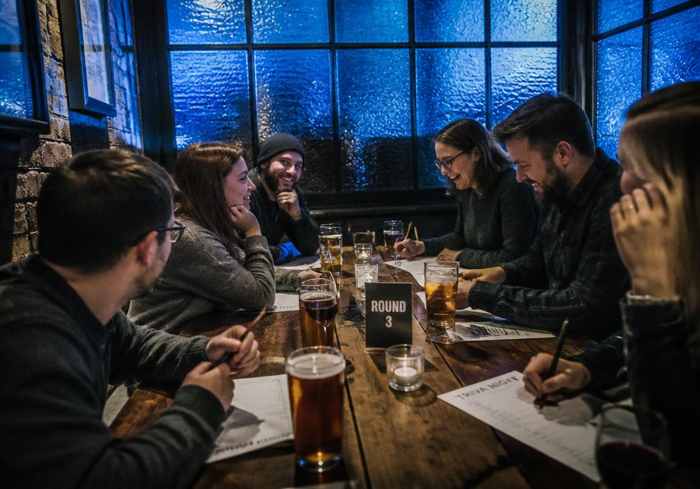 Friends laughing over pints and answer sheets on trivia night at Bellevue Cellars